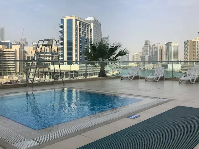 A rooftop swimming pool with lounge seating and city buildings in the background.