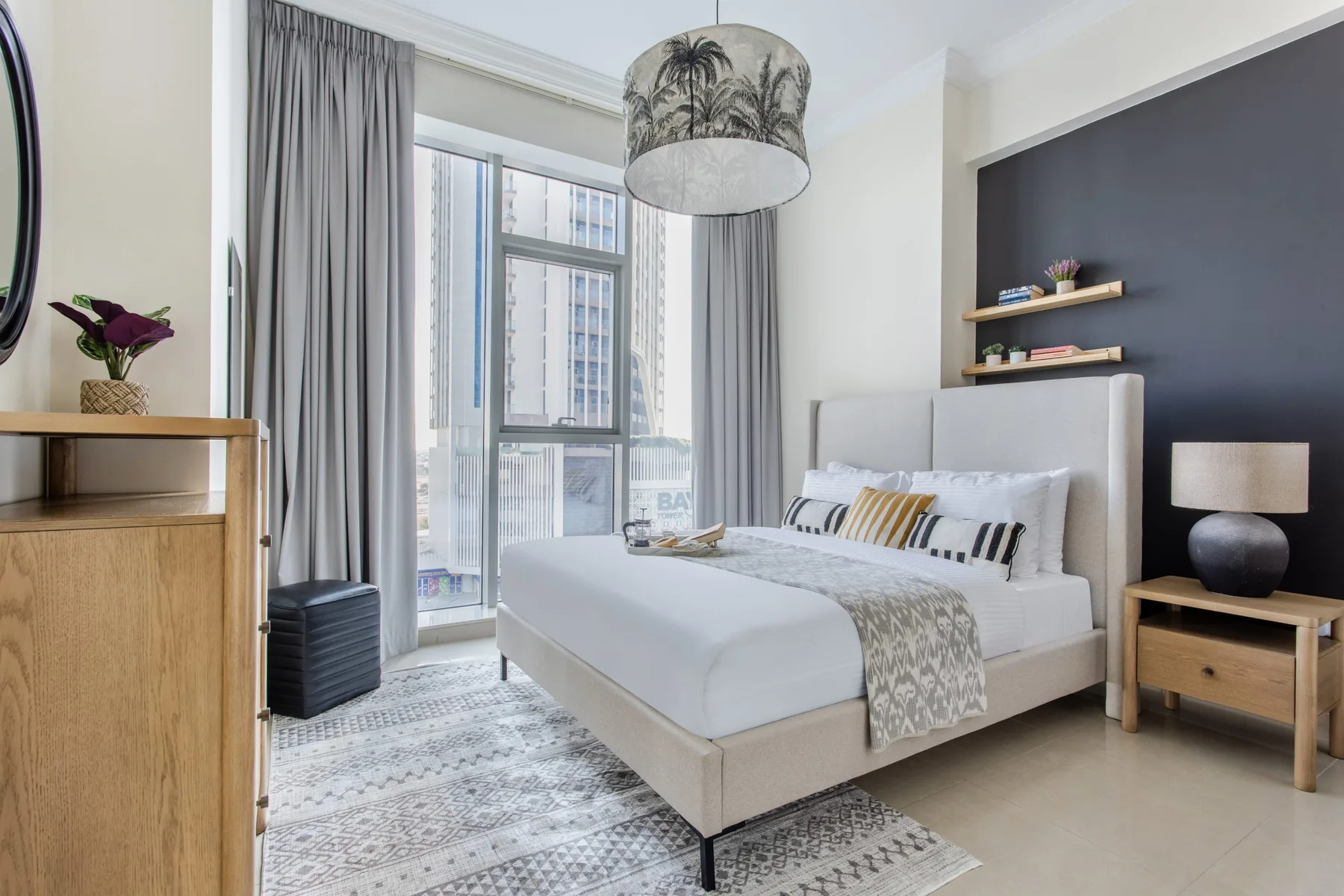 A bright bedroom with a neatly made bed beside tall windows and gray curtains.
