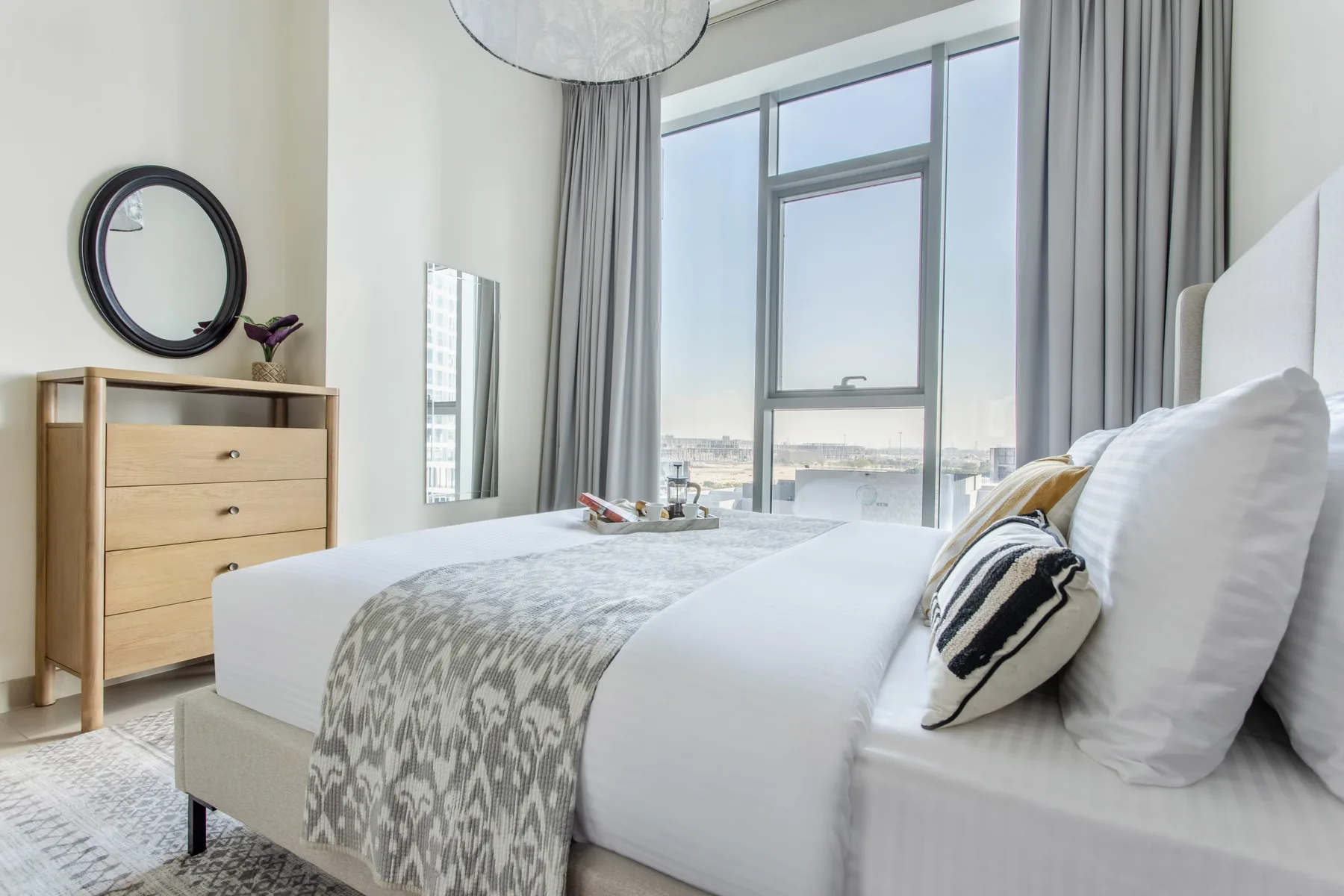 A bright bedroom with a neatly made bed beside a large window.