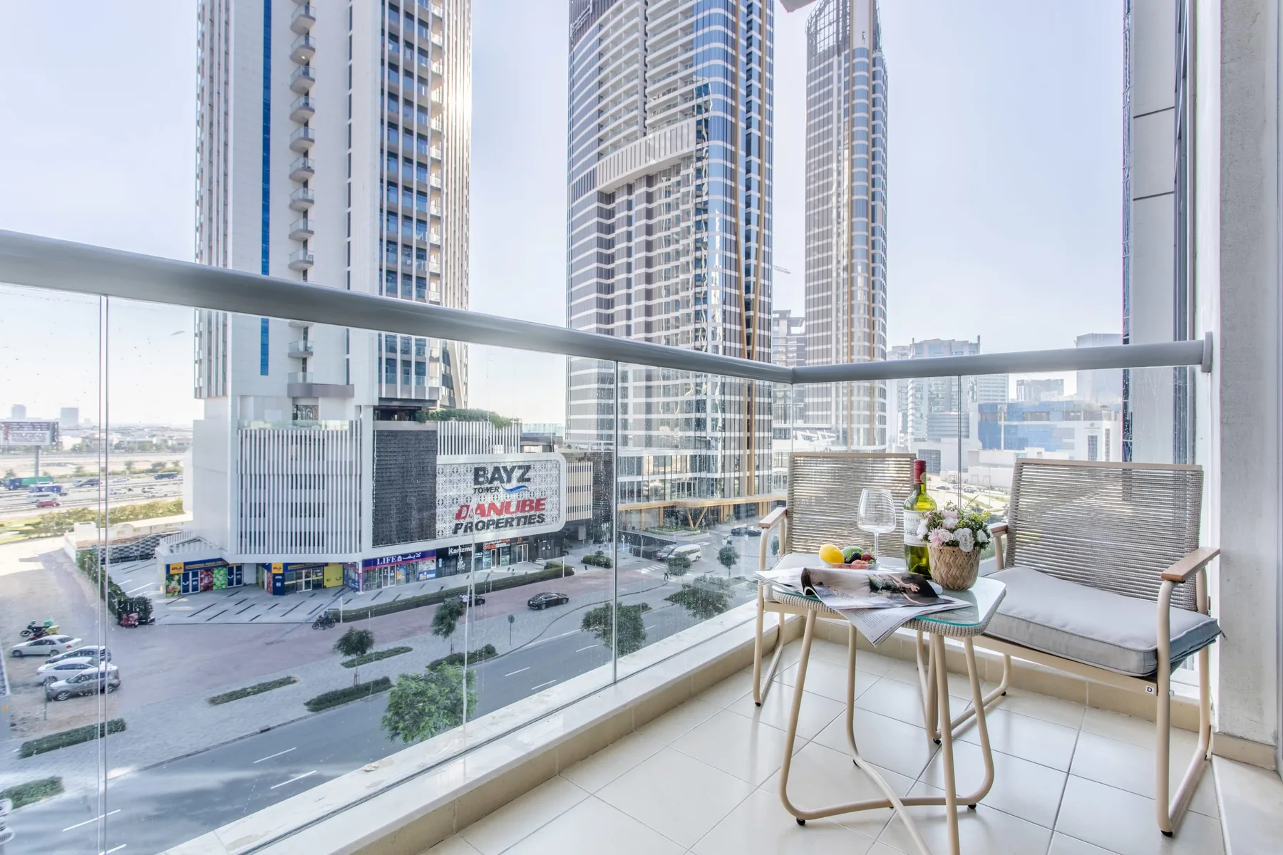 A balcony seating area with a small table overlooks surrounding high-rise buildings.