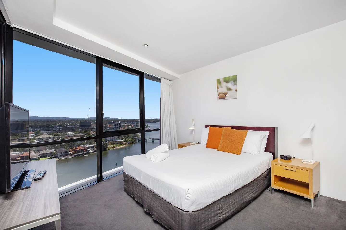 A bright bedroom with a bed beside large windows overlooking a river.