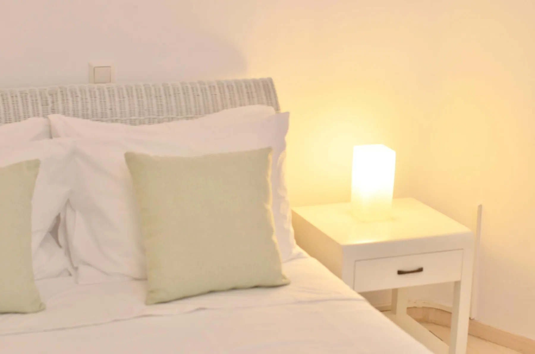 A bedroom with a neatly made bed and a lit bedside lamp.