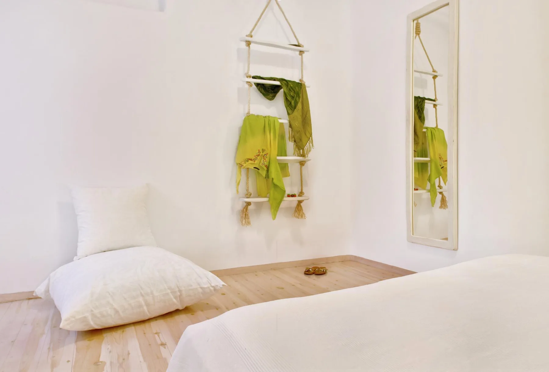A bright bedroom with white bedding and a wall mirror.