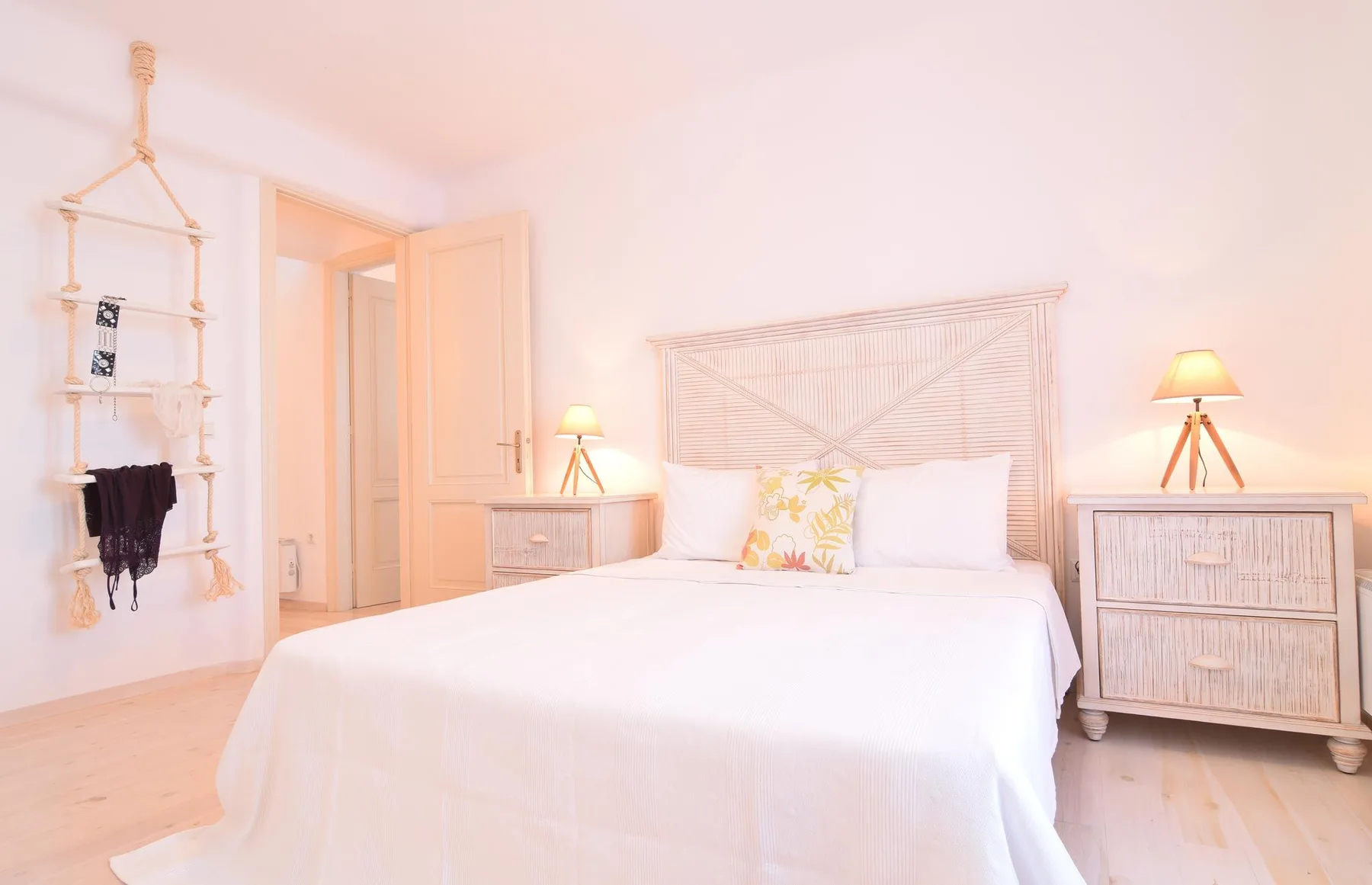 A bright bedroom with a bed, bedside lamps, and woven headboard.