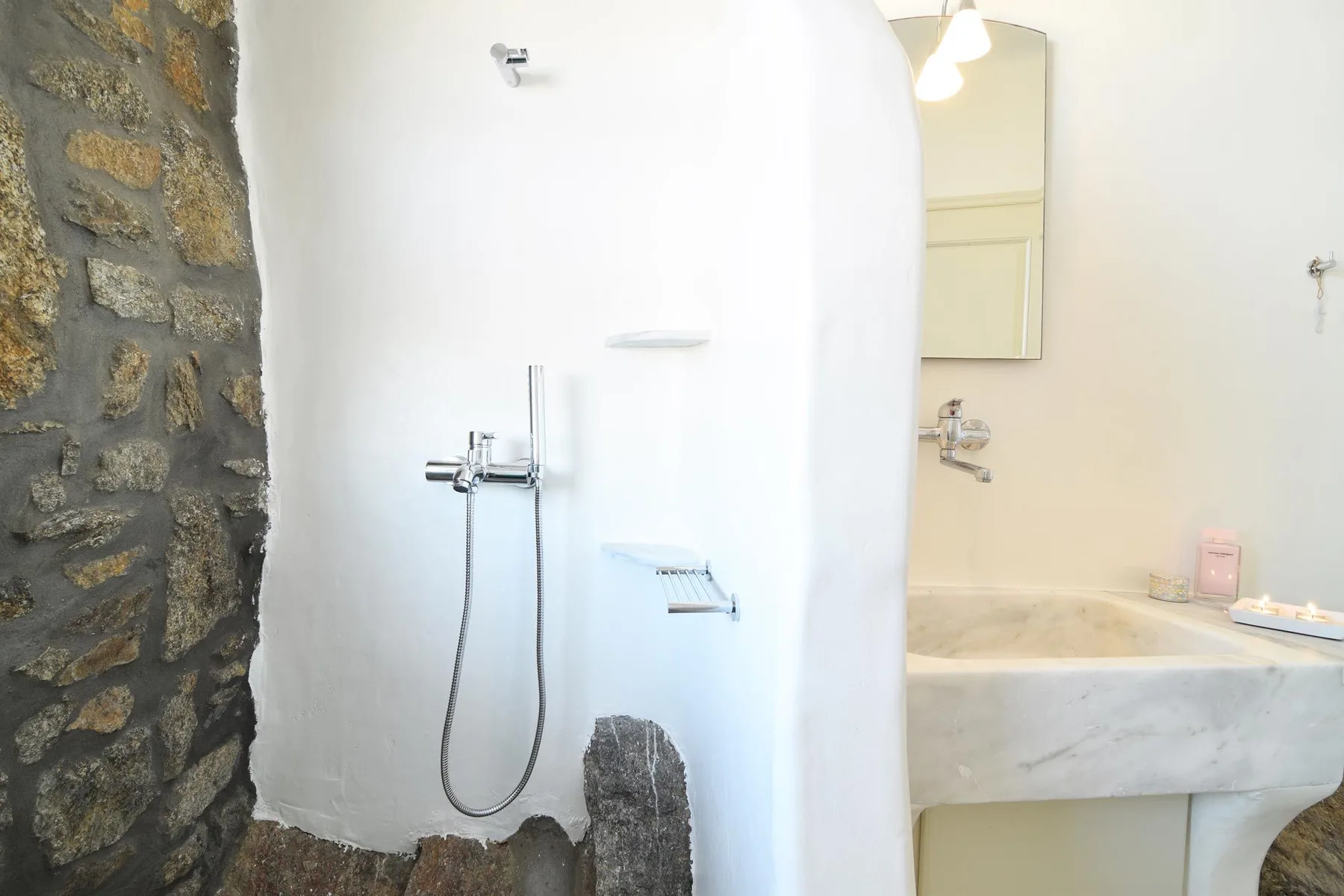 A bathroom shower beside a stone wall and a marble sink.