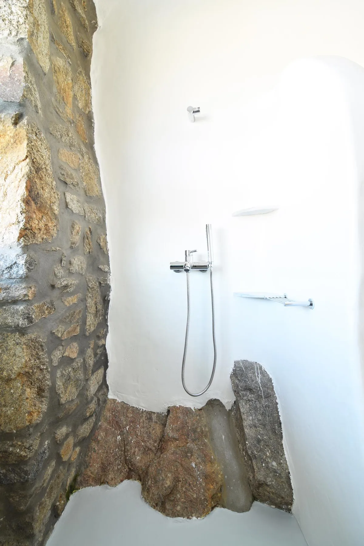 A shower with a stone wall and exposed rock along the base.