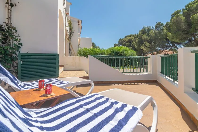 Una terraza soleada al aire libre con asientos a rayas y barandillas verdes.
