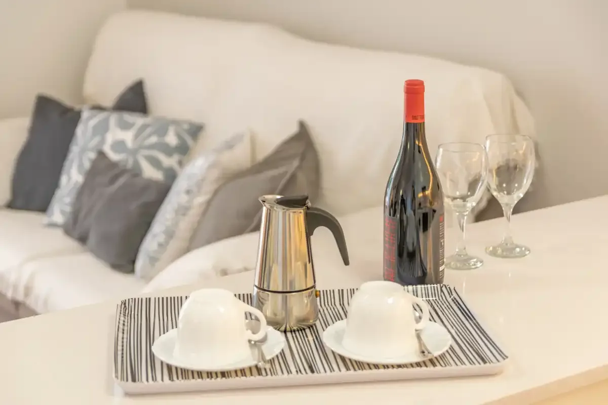 Una zona de estar con una bandeja que contiene tazas, una cafetera y copas de vino.