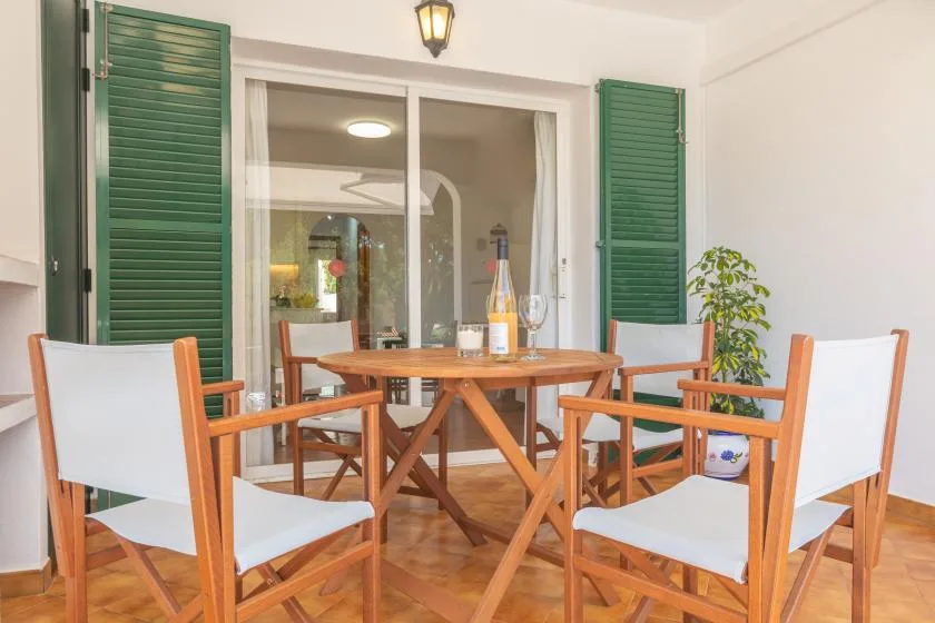 Un comedor en el patio con asientos de madera alrededor de una mesa junto a persianas verdes.