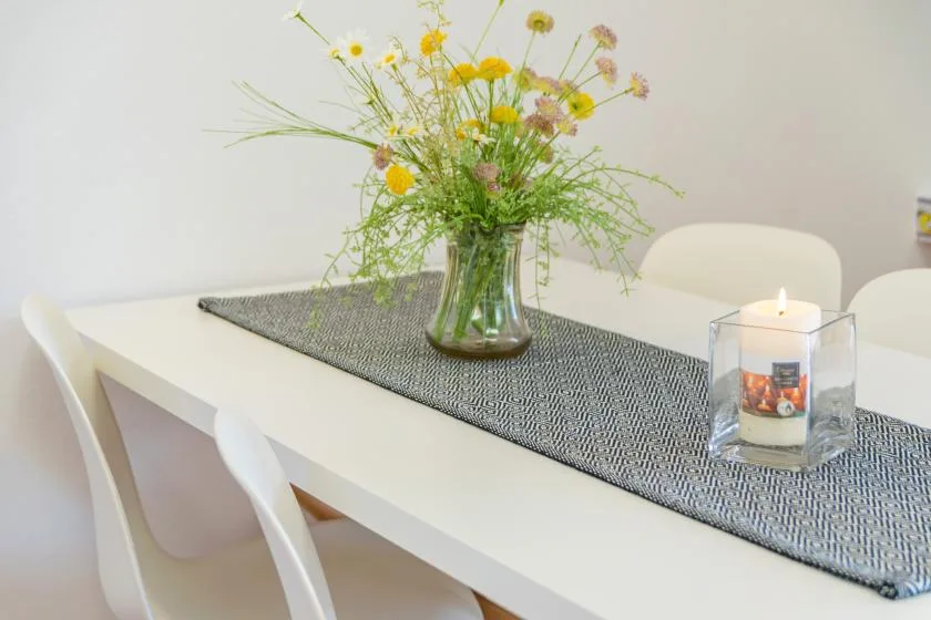 Una mesa de comedor con un jarrón de flores y una vela encendida.