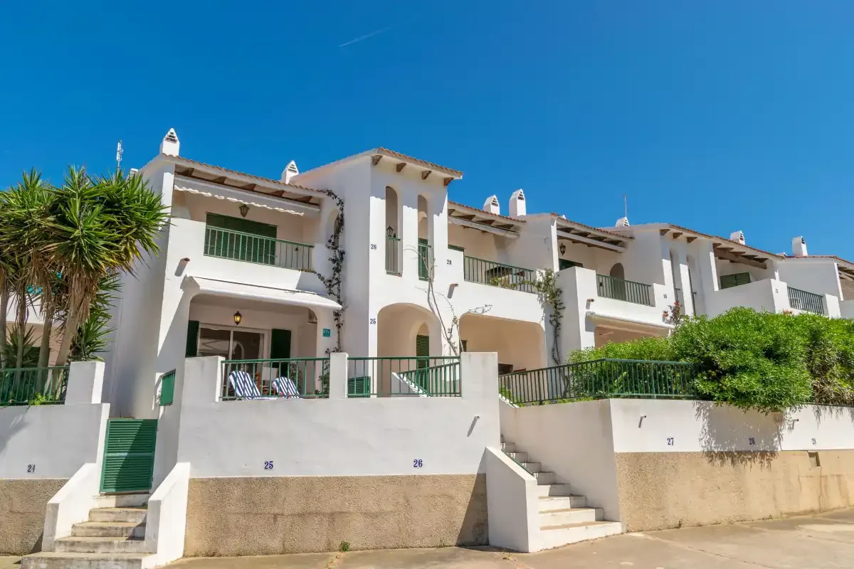 Una fila de casas adosadas blancas con balcones y escalones al frente bajo un cielo azul despejado.