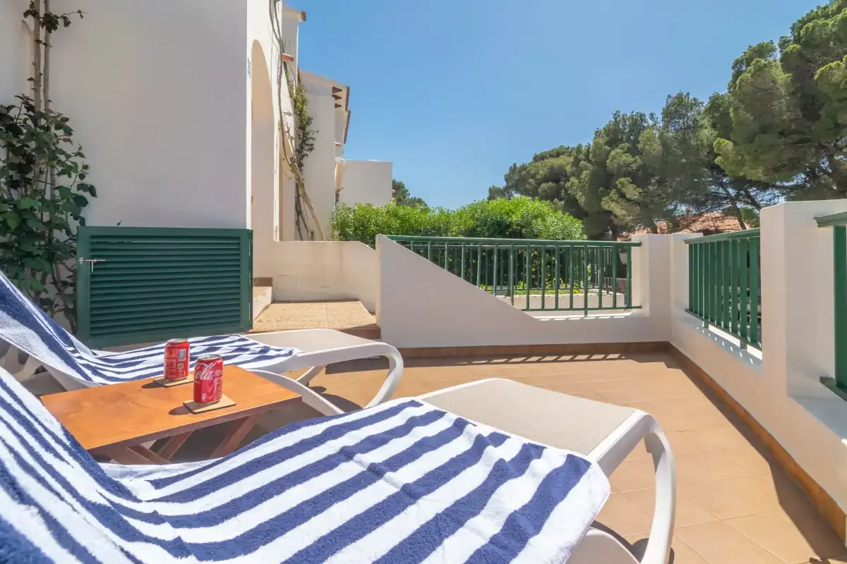 Una terraza soleada con tumbonas a rayas y barandillas verdes.