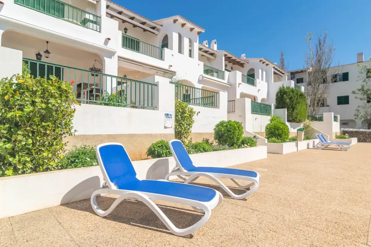Un patio soleado con tumbonas azules junto a edificios de apartamentos blancos.