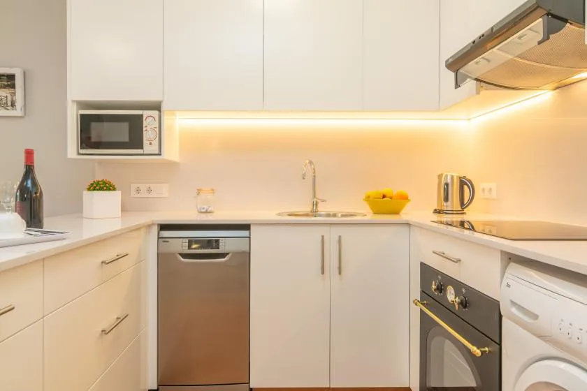 Una cocina luminosa con gabinetes blancos, una encimera y electrodomésticos de acero inoxidable.