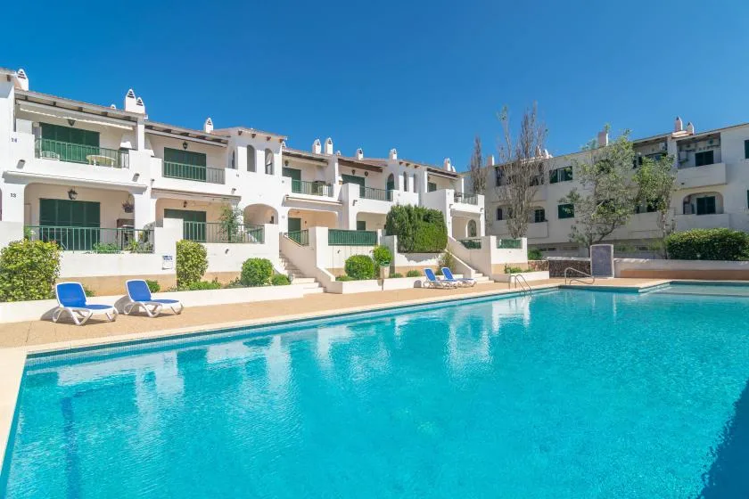 Una piscina rodeada de edificios de apartamentos blancos y asientos de descanso.