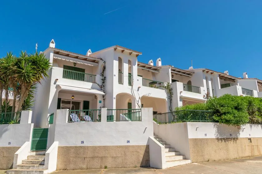 Edificios residenciales blancos de varios niveles con balcones se alzan bajo un cielo azul despejado.