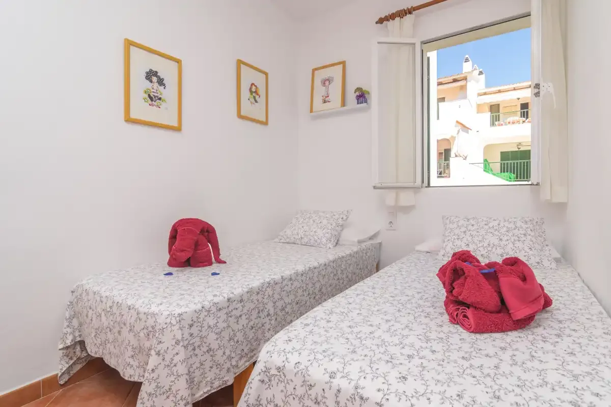 Un dormitorio con dos camas individuales y una ventana con vistas a edificios vecinos.