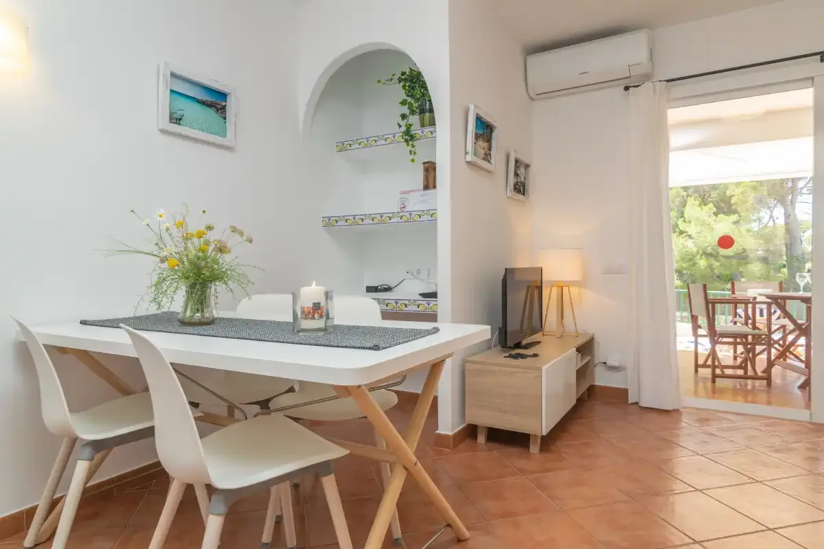 Un comedor luminoso con una mesa y sillas junto a un hueco de cocina en arco.