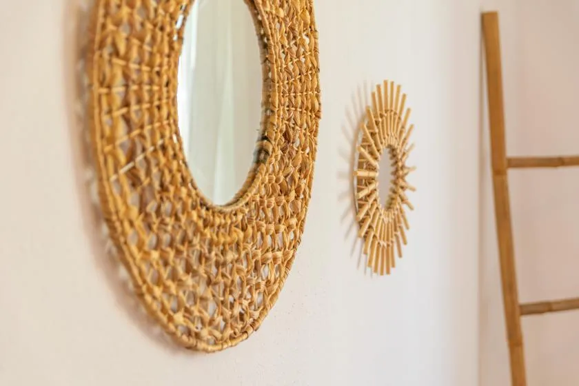Un espejo ovalado tejido y una decoración pequeña en forma de sol cuelgan de una pared clara.