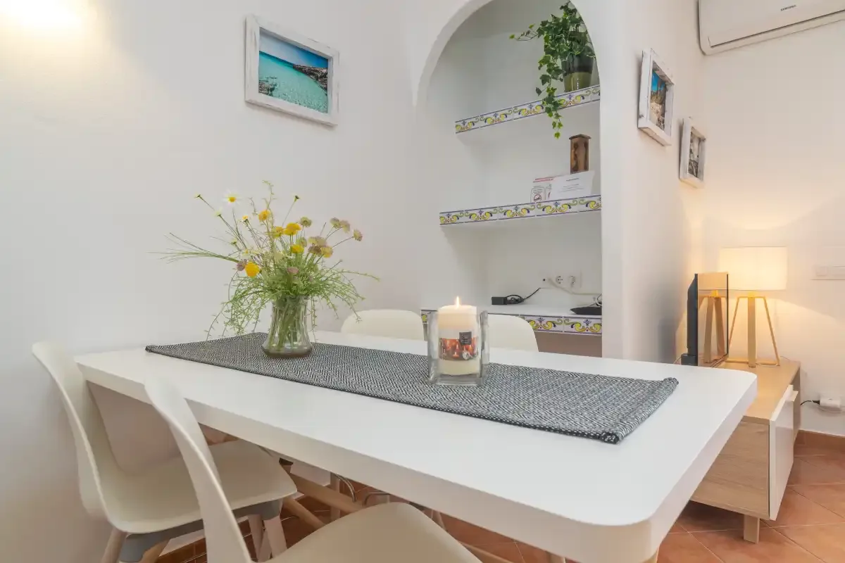 Comedor con una mesa blanca, sillas y un jarrón con flores.