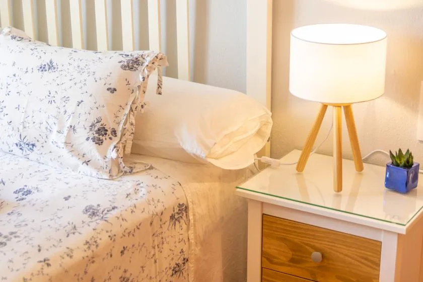 Un dormitorio con una cama floral junto a una lámpara de mesa encendida.