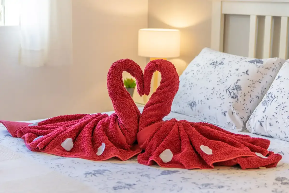 Una cama de dormitorio está decorada con toallas rojas dispuestas en forma de corazón.