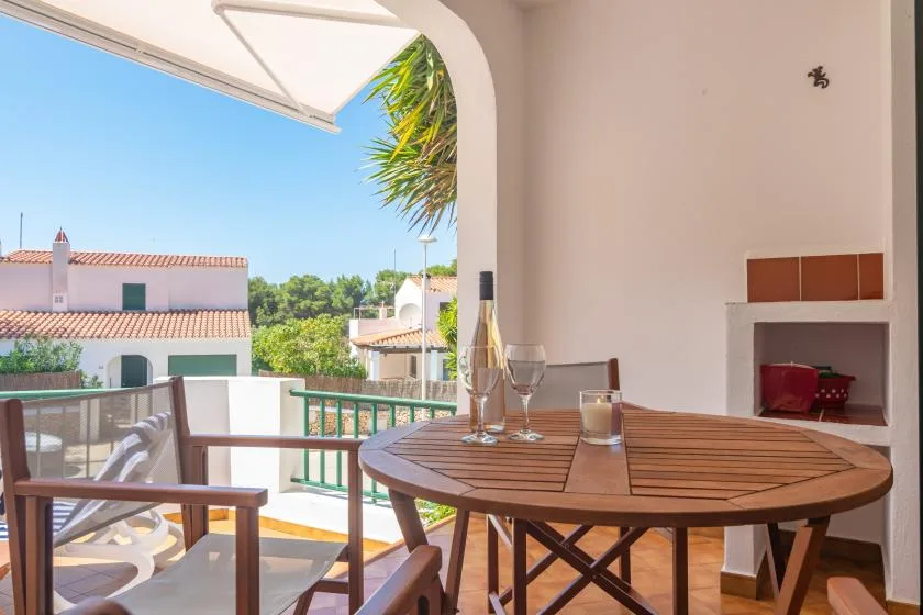 Una luminosa zona de comedor en el balcón, con una mesa redonda de madera y vistas a edificios cercanos.