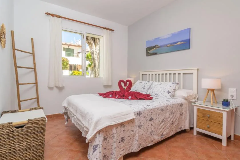 Un dormitorio luminoso con una cama bajo un cuadro de paisaje costero.