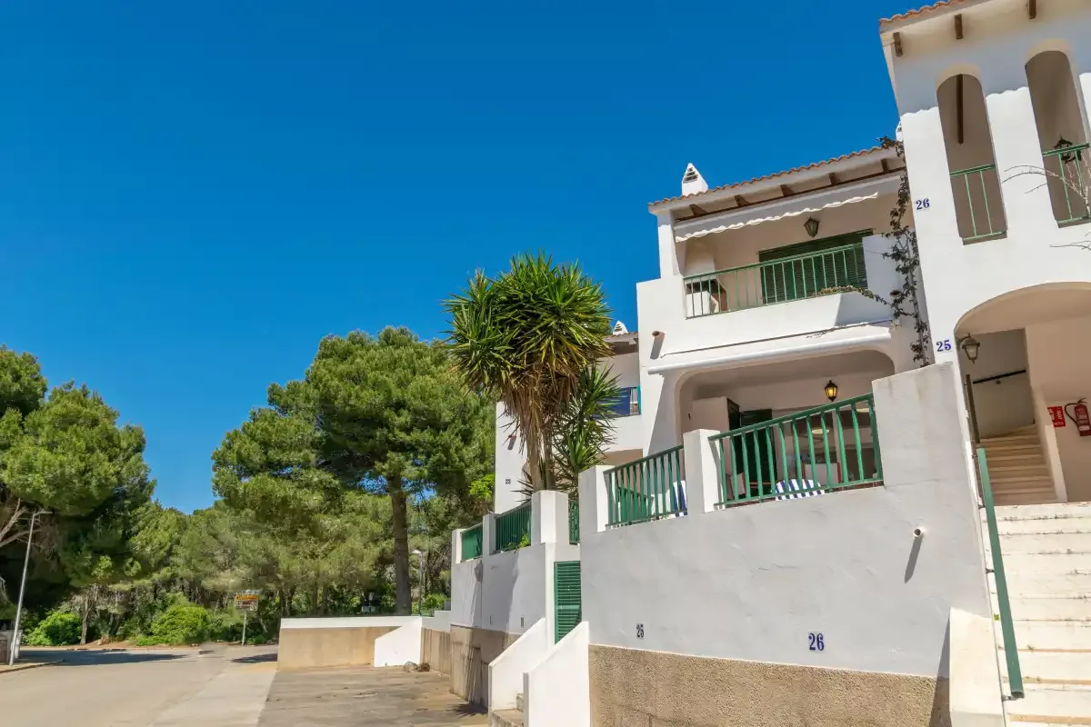 Edificios residenciales blancos con barandillas verdes junto a una carretera arbolada.