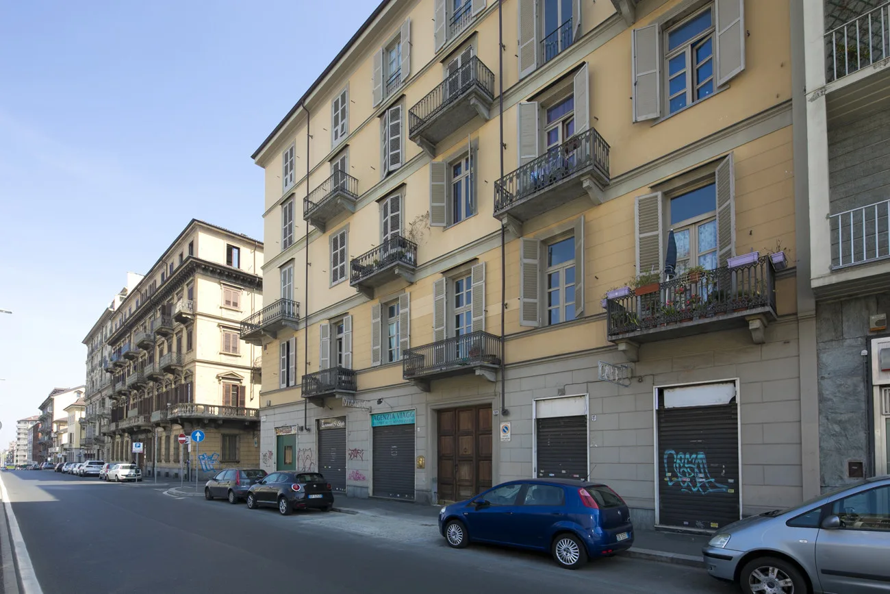 Una calle urbana flanqueada por edificios de varias plantas y coches aparcados.