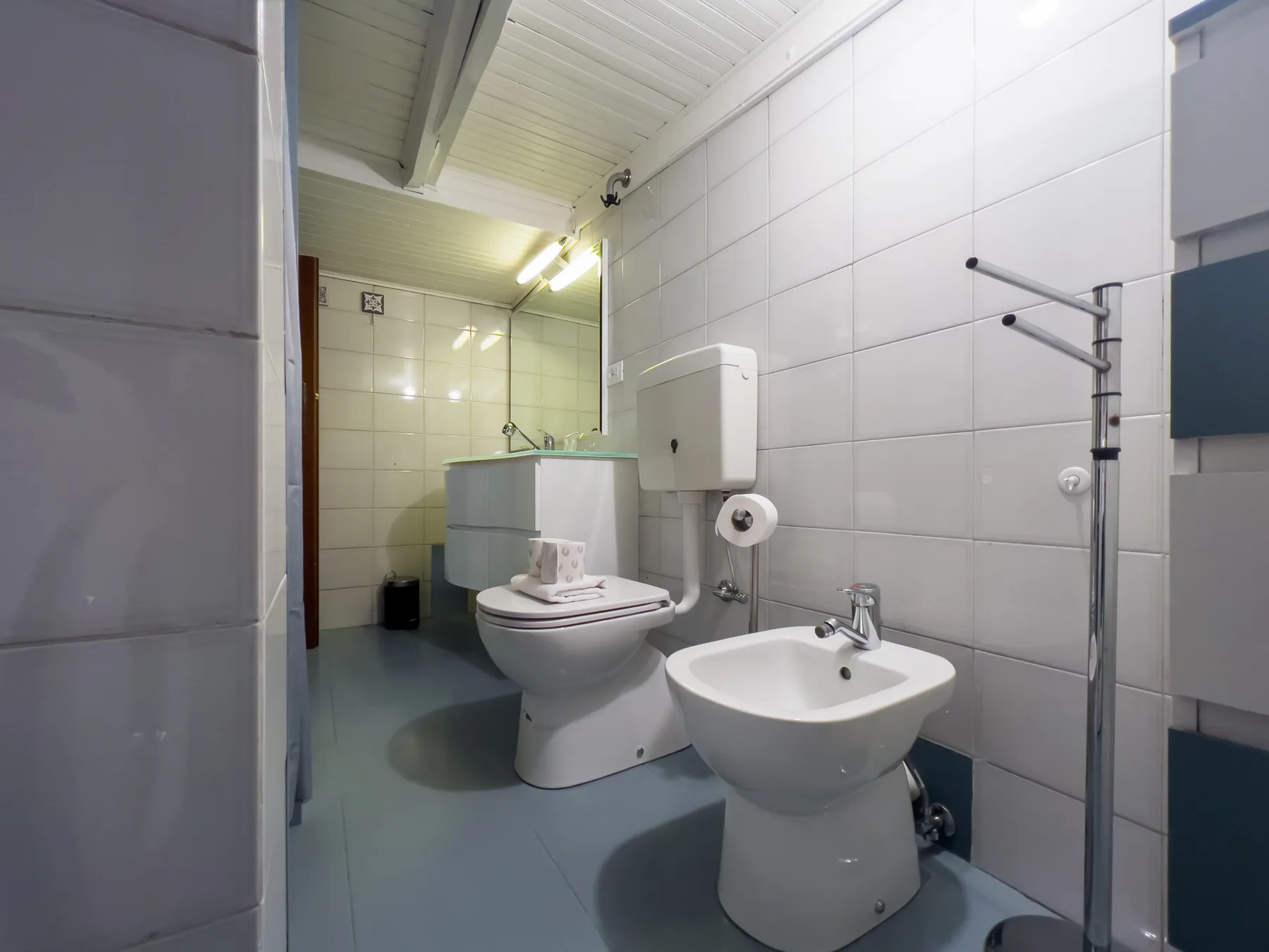 Un baño con azulejos, un inodoro y un lavabo bajo un techo inclinado.