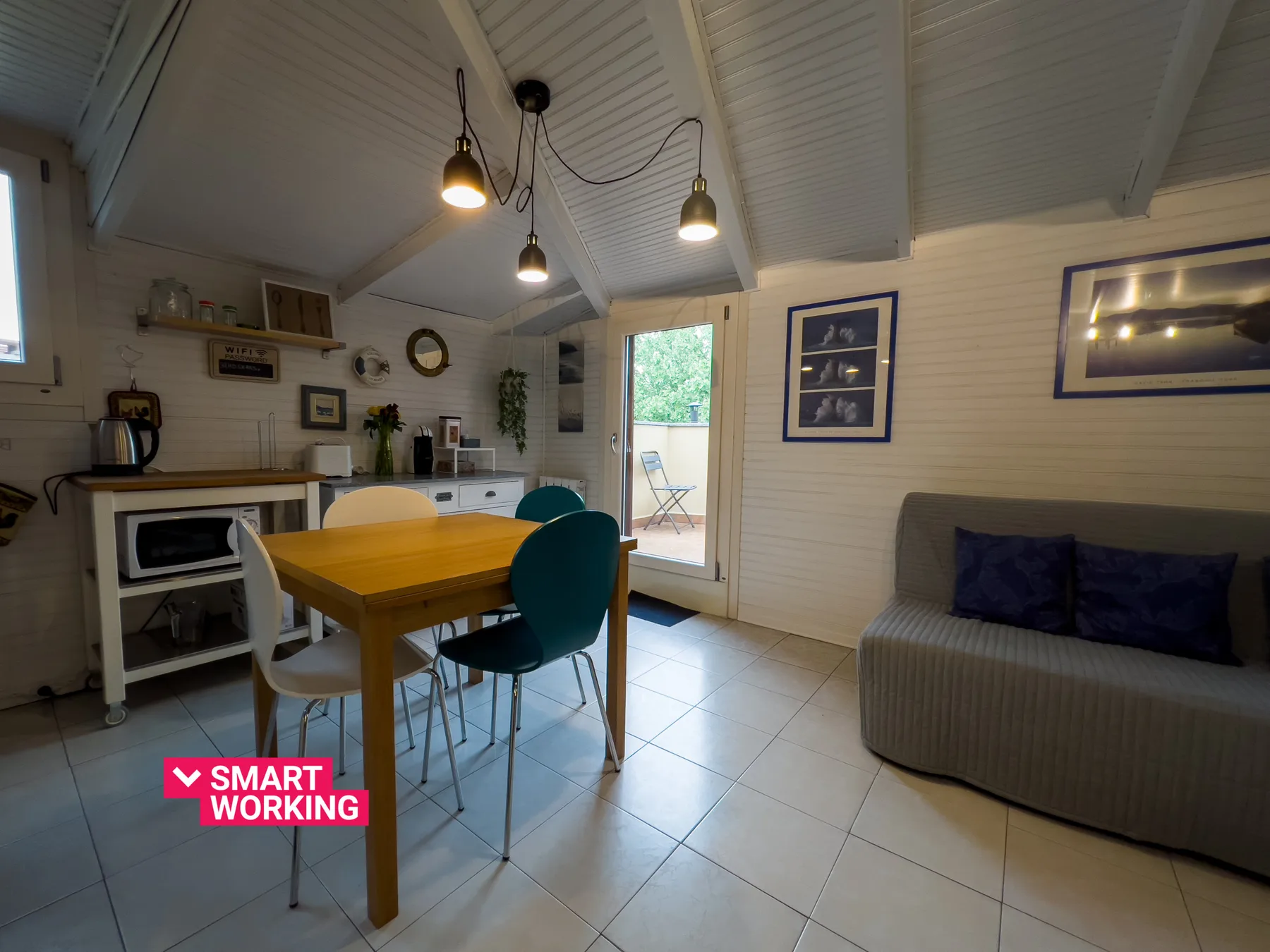Una luminosa zona de comedor y estar con una mesa de madera y asientos grises.