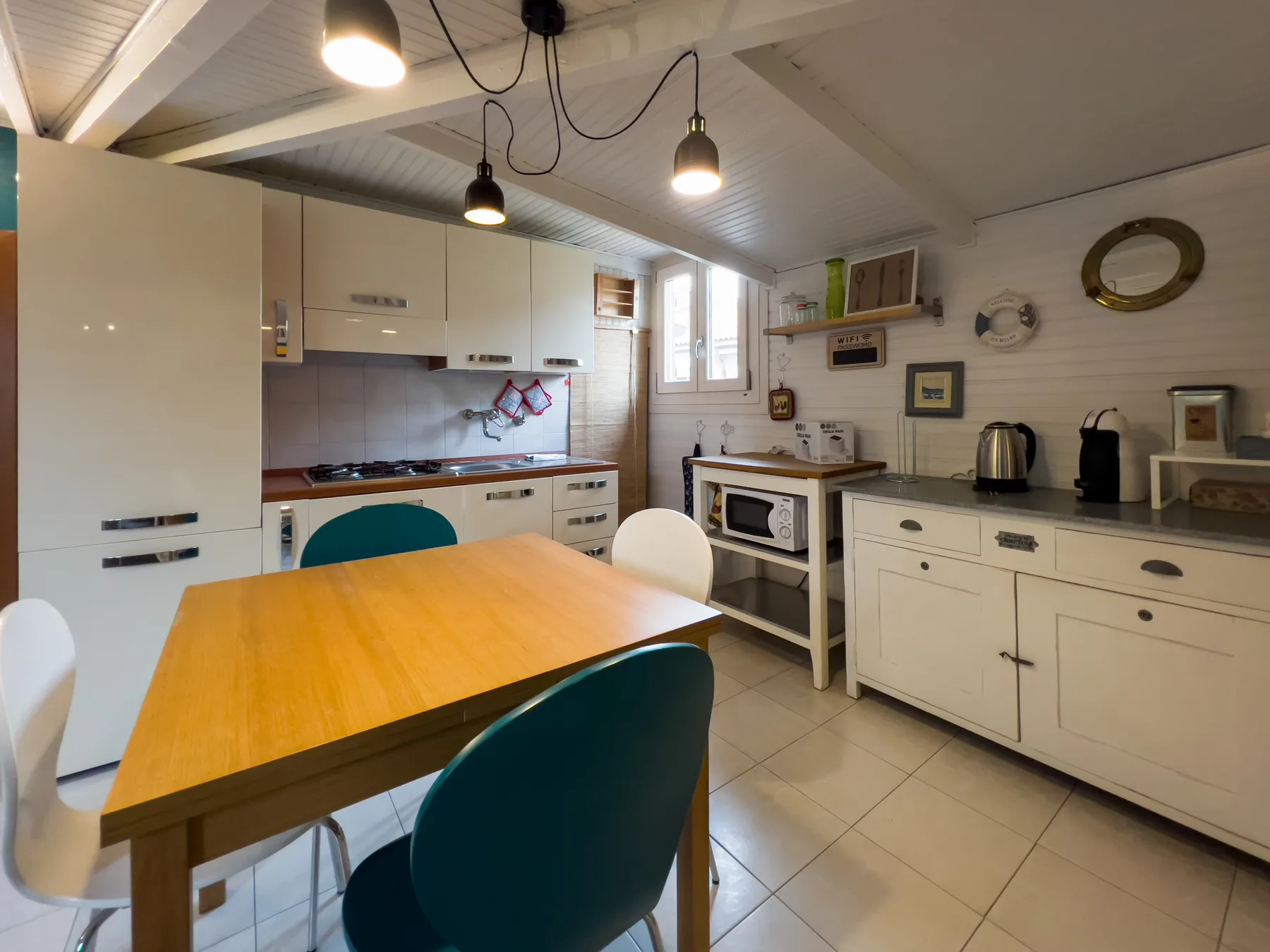 Una cocina y comedor con una mesa de madera, armarios blancos y lámparas colgantes.