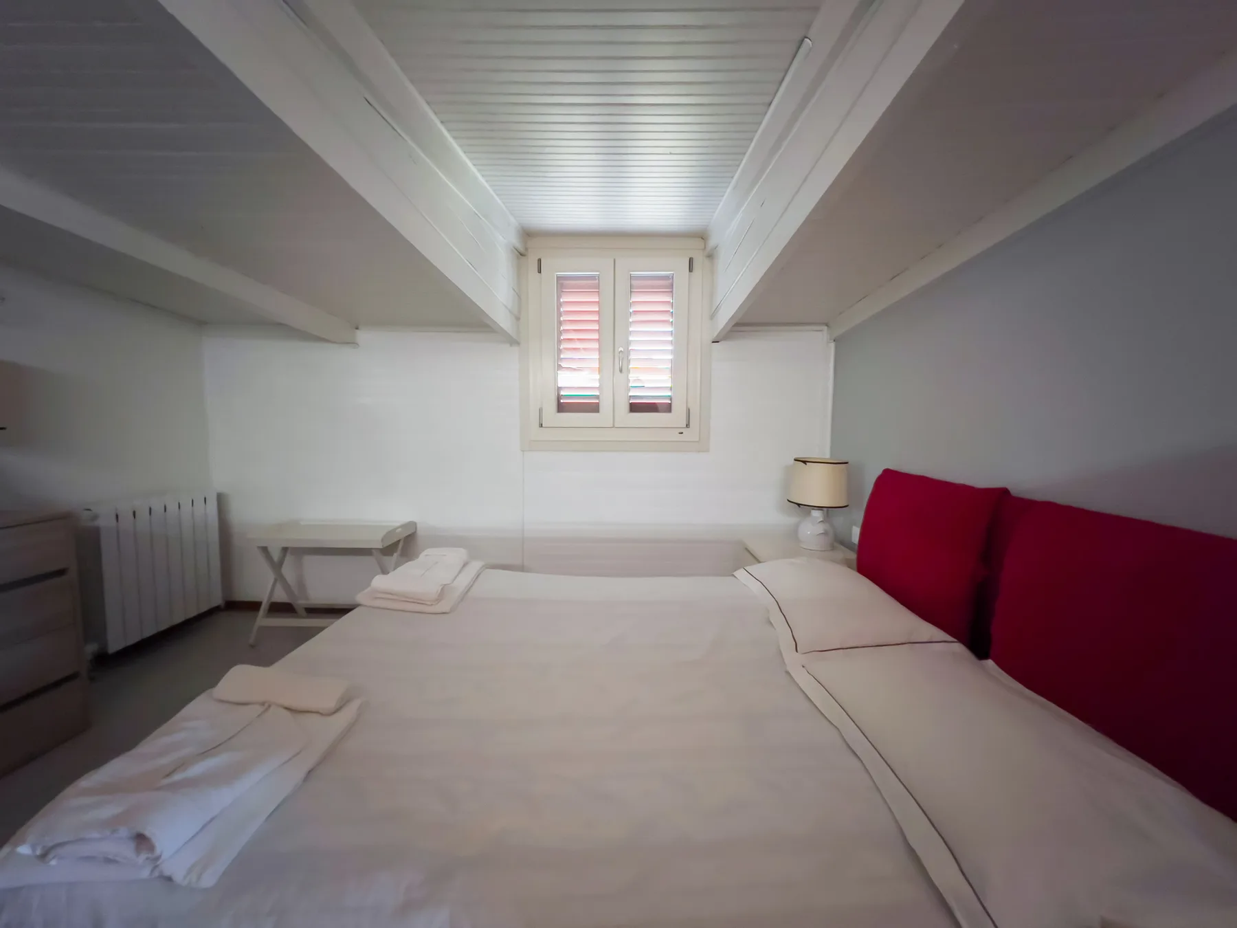 Un dormitorio con una cama, almohadas rojas y una ventana pequeña.