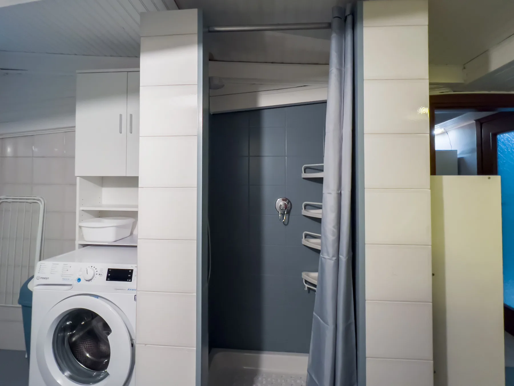 Un baño con una lavadora junto a una zona de ducha y una cortina.