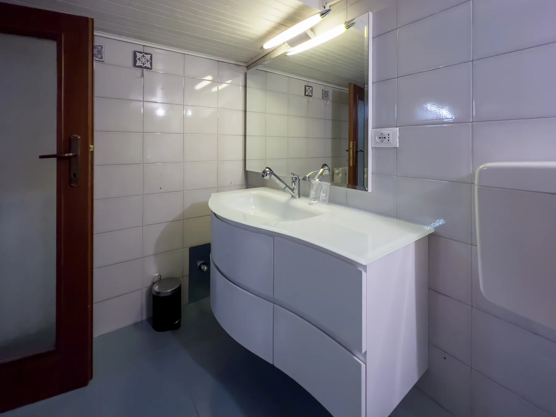 Un baño alicatado con un lavabo curvo, espejo e iluminación superior.