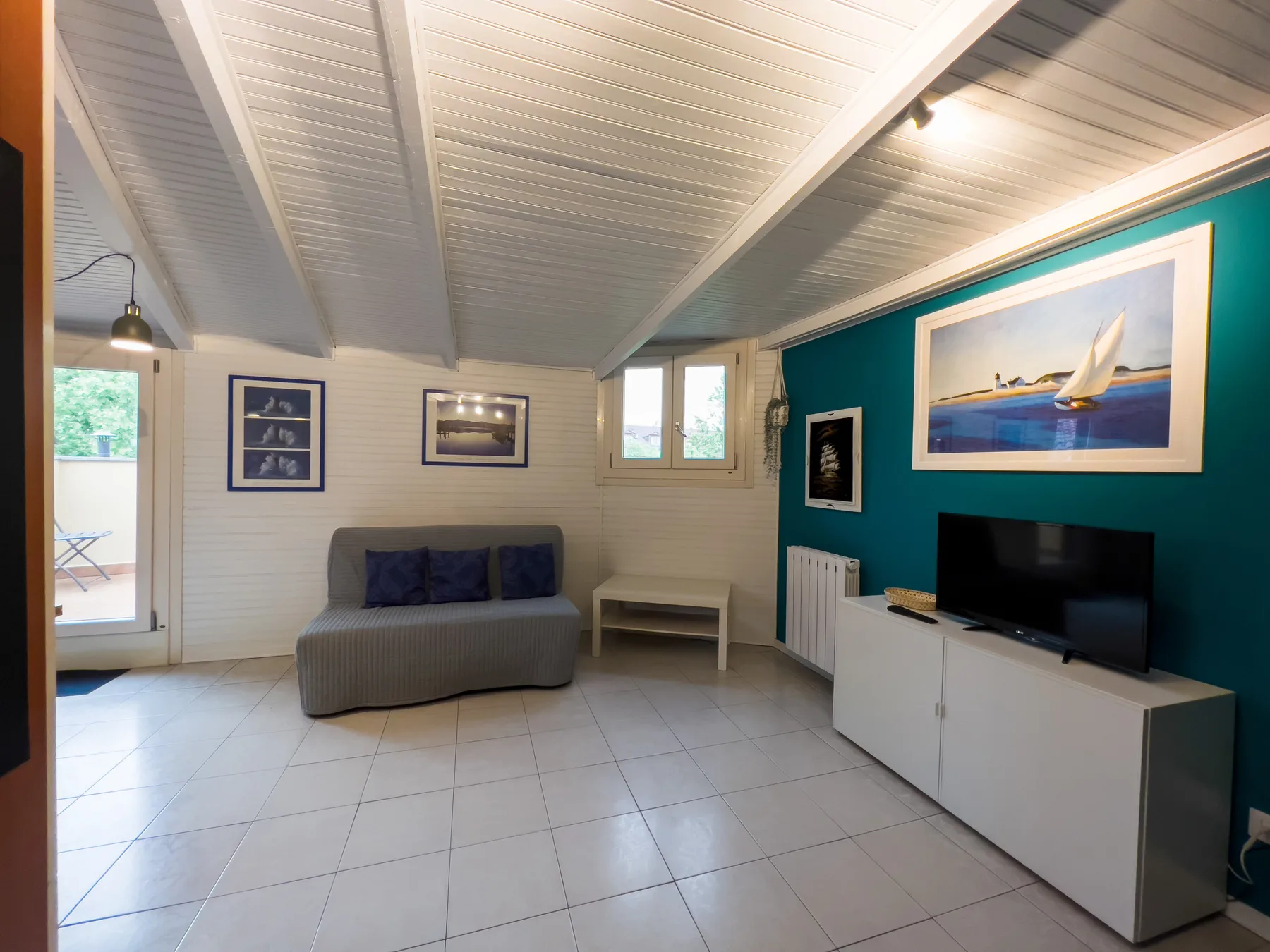 Una sala de estar luminosa con un sofá y un televisor junto a una pared verde azulado.