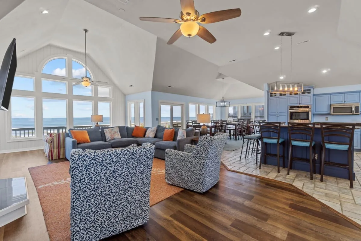 An open-plan living room and kitchen with seating, a dining area, and large windows.
