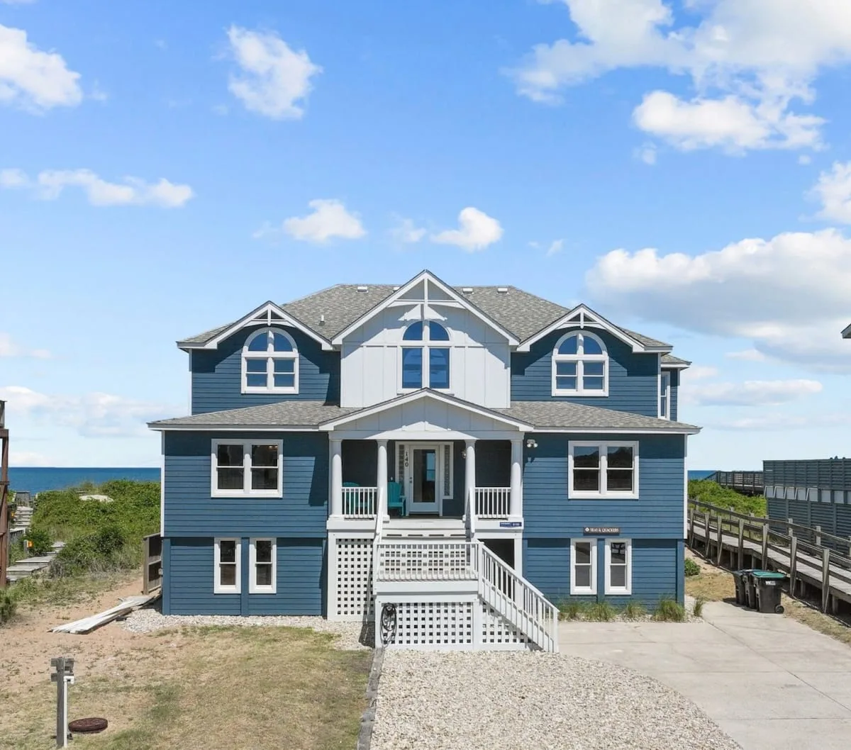 A blue coastal house with white trim stands beside a gravel driveway.