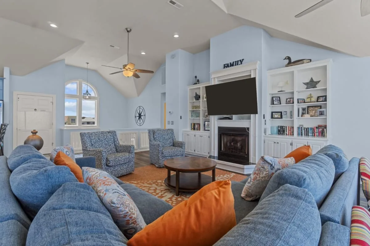 A spacious living room with blue seating arranged around a fireplace and television.