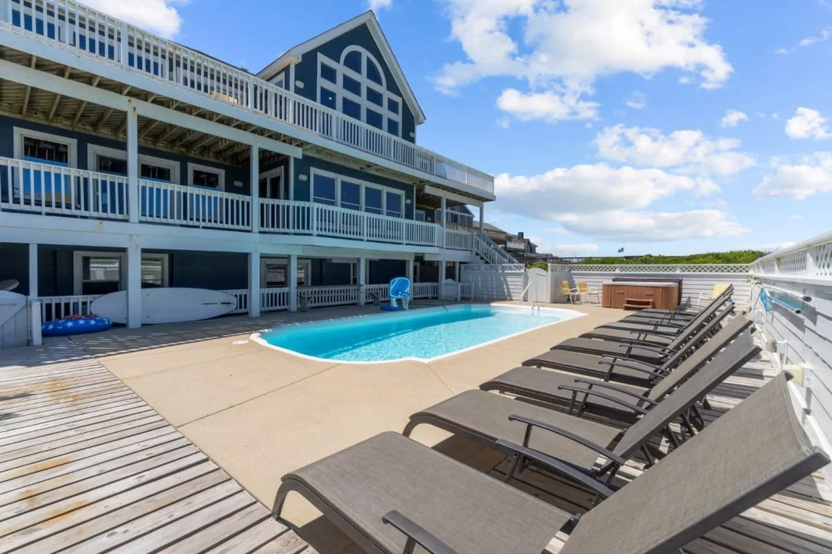 An outdoor pool beside a large multi-level building, with loungers along the deck.
