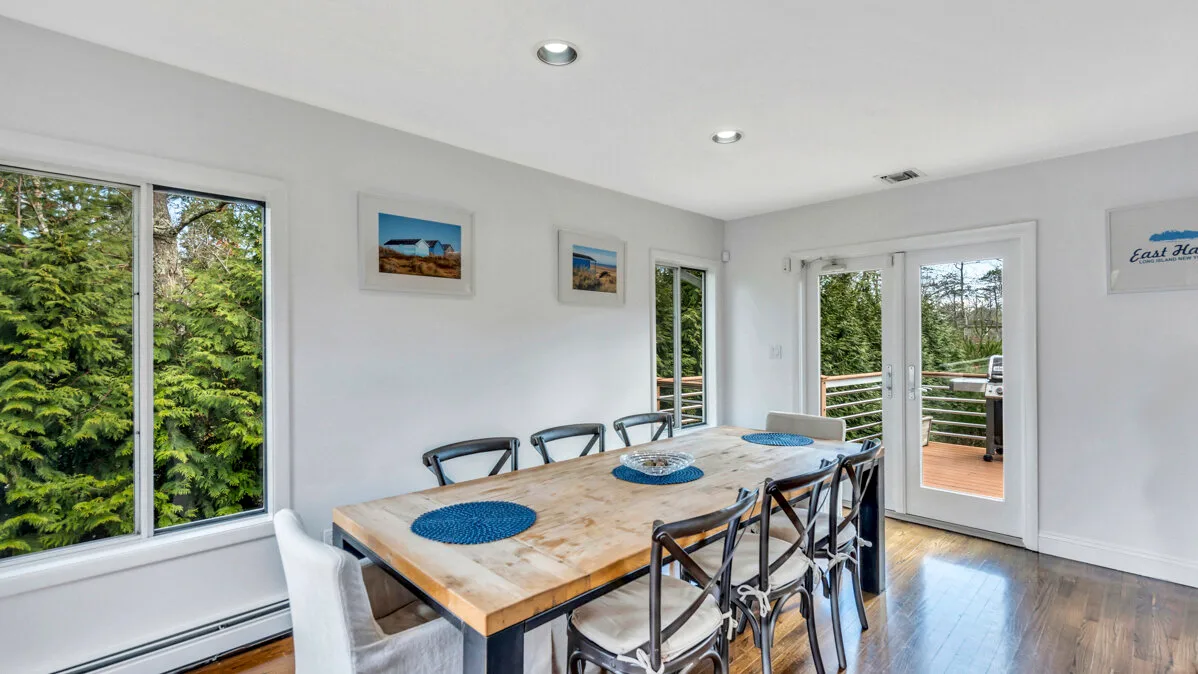 A bright dining area with a long table beside large windows and a glass door.