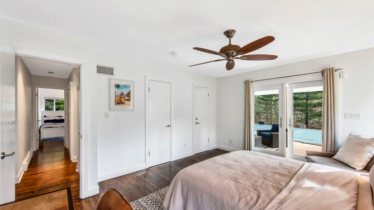 A bedroom with a bed, ceiling fan, and sliding glass doors opening toward a pool.