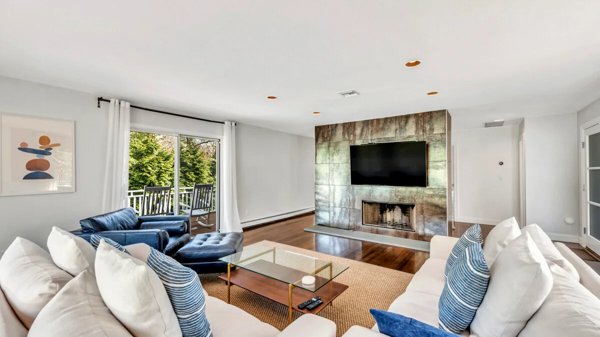 A bright living room with seating around a glass coffee table and fireplace.