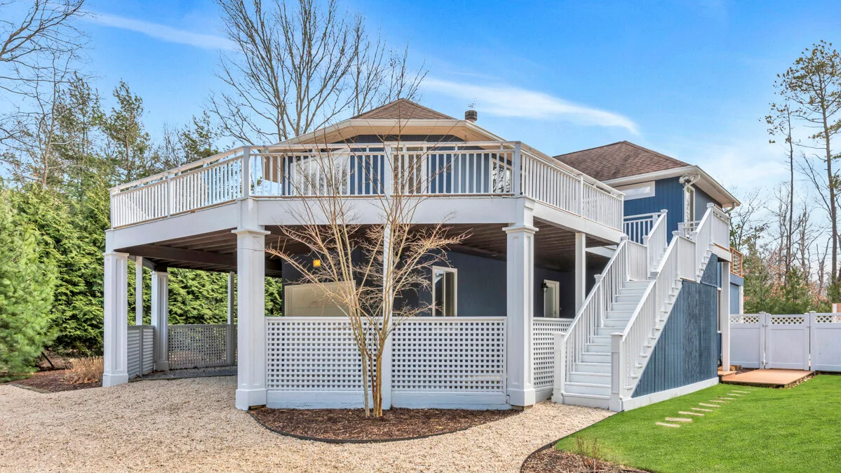 Raised house deck with white railings, stairs, and a gravel patio.
