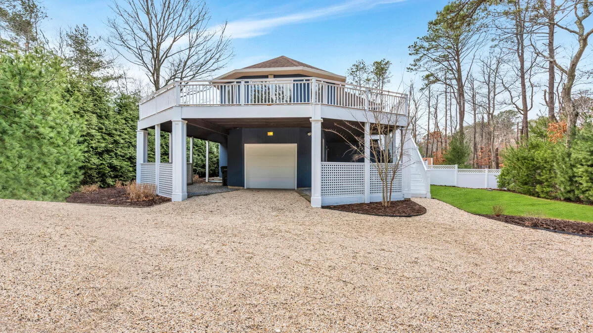 A raised outdoor deck with white railings stands above a covered parking area.