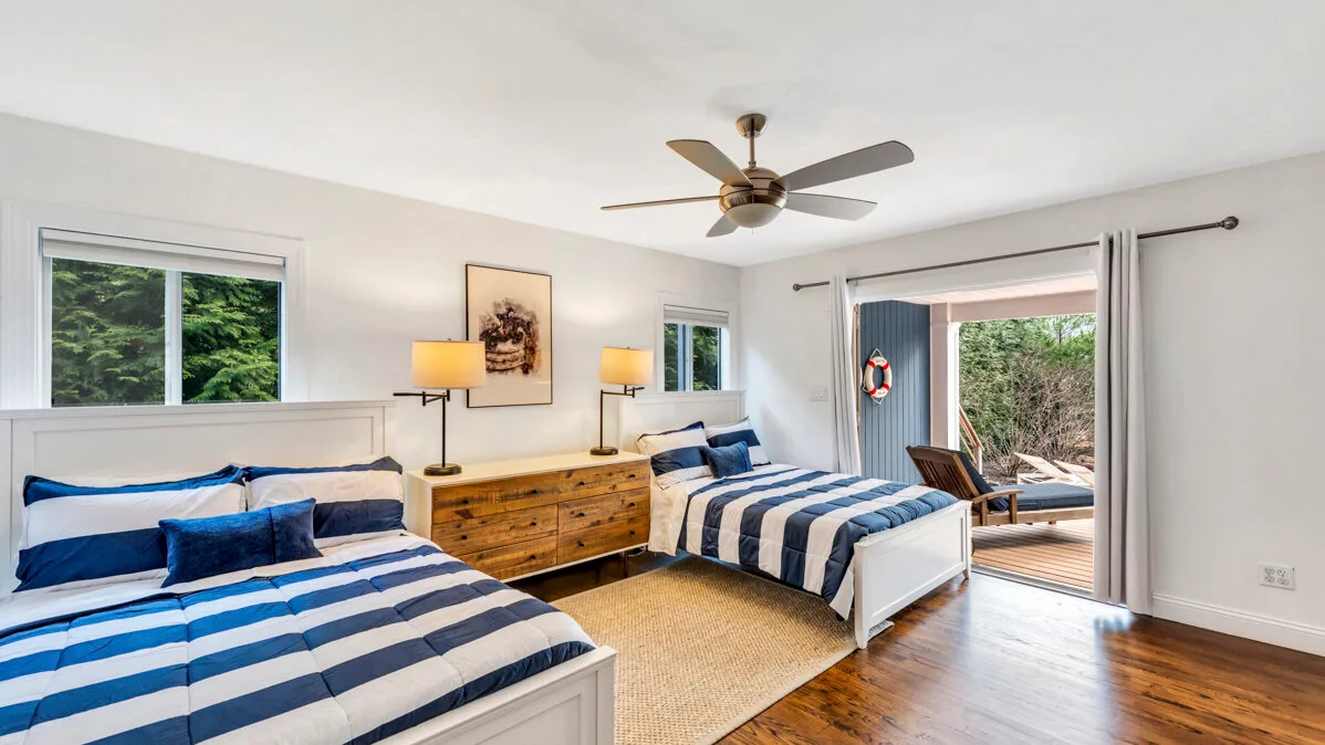 A bright bedroom with two beds, striped bedding, and a ceiling fan.