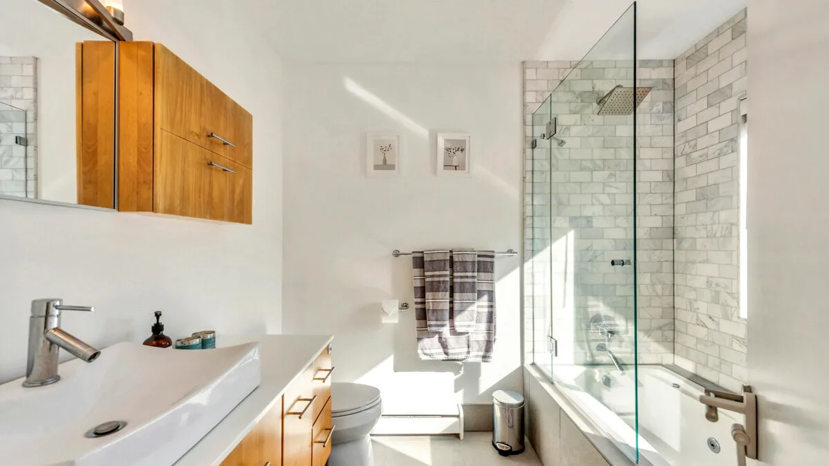 A bright bathroom with a long sink, toilet, and glass shower.