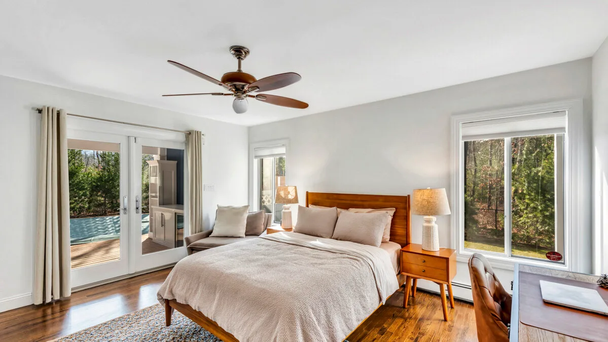 A bright bedroom with a bed, bedside tables, and windows overlooking greenery.