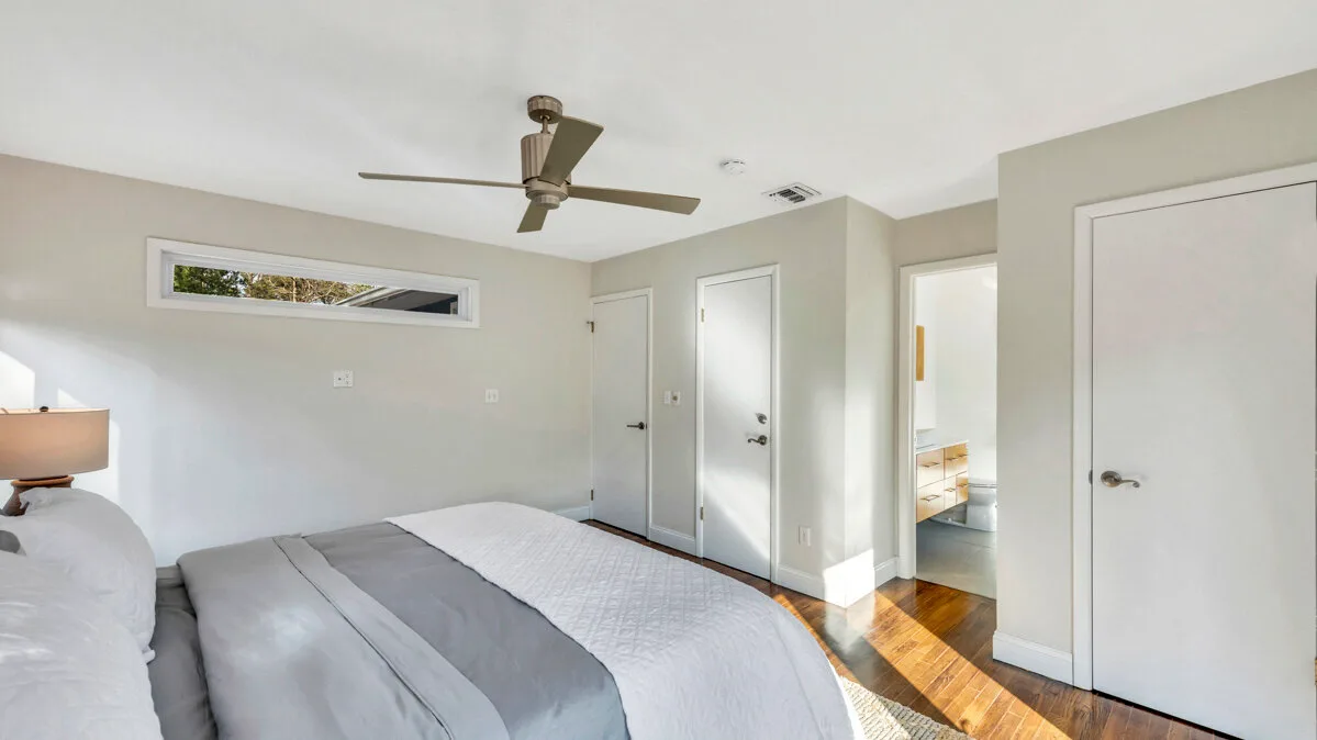 A bright bedroom with a bed, ceiling fan, and several doors.